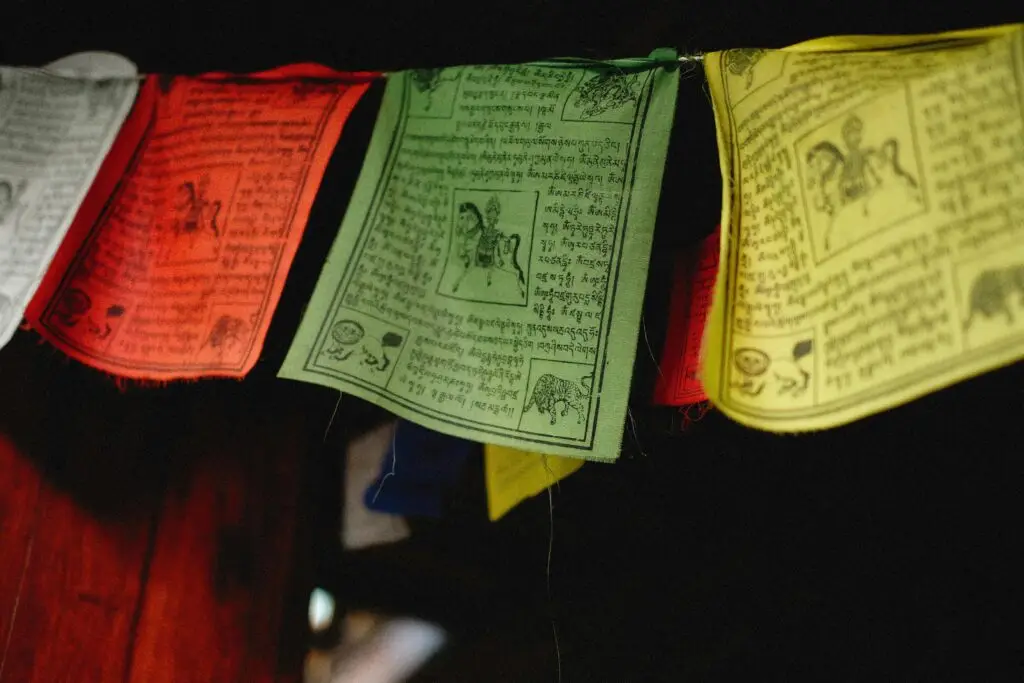 A close-up of colorful Tibetan prayer flags hanging indoors, featuring intricate designs and text.
